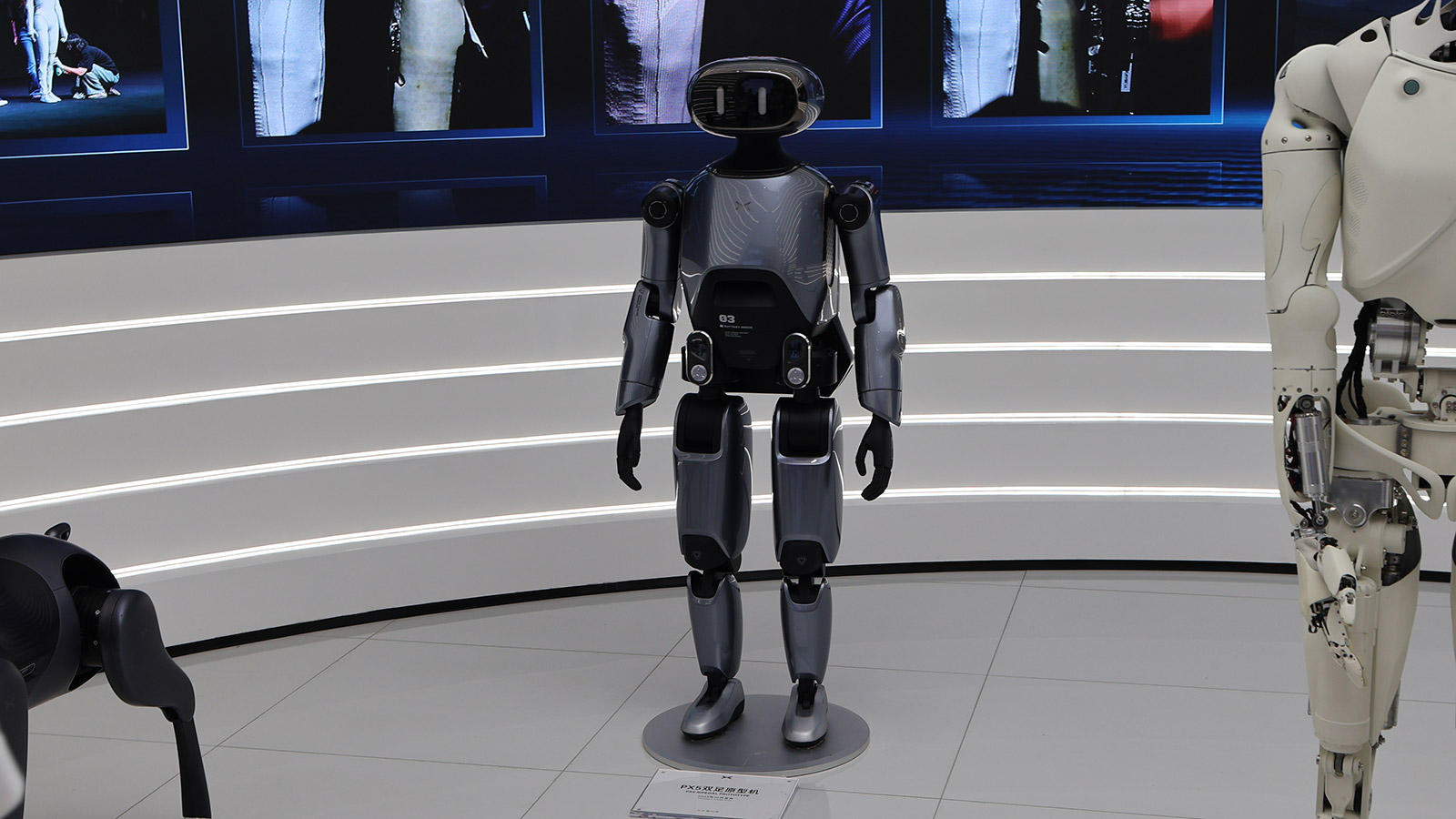 A dark gray Xpeng humanoid robot stands alongside other robots in a display area at the company's Guangzhou headquarters.