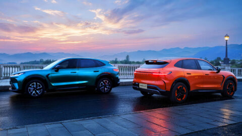 Teal and orange Arcfox Alpha T7 SUVs parked facing opposite directions on a wet terrace at sunset, with mountains in the background.