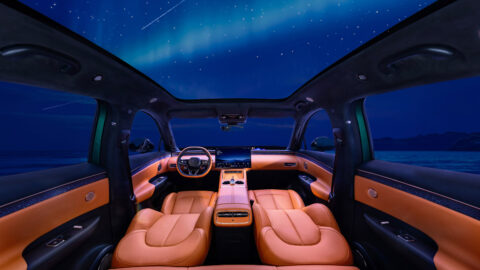 Wide view of the Arcfox Alpha T7’s orange-and-black cabin, showing the reclined front seats and panoramic glass roof.