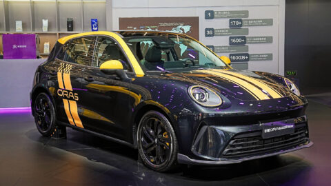 A black GWM Ora 5 Sport with yellow racing stripes displayed at a launch venue.