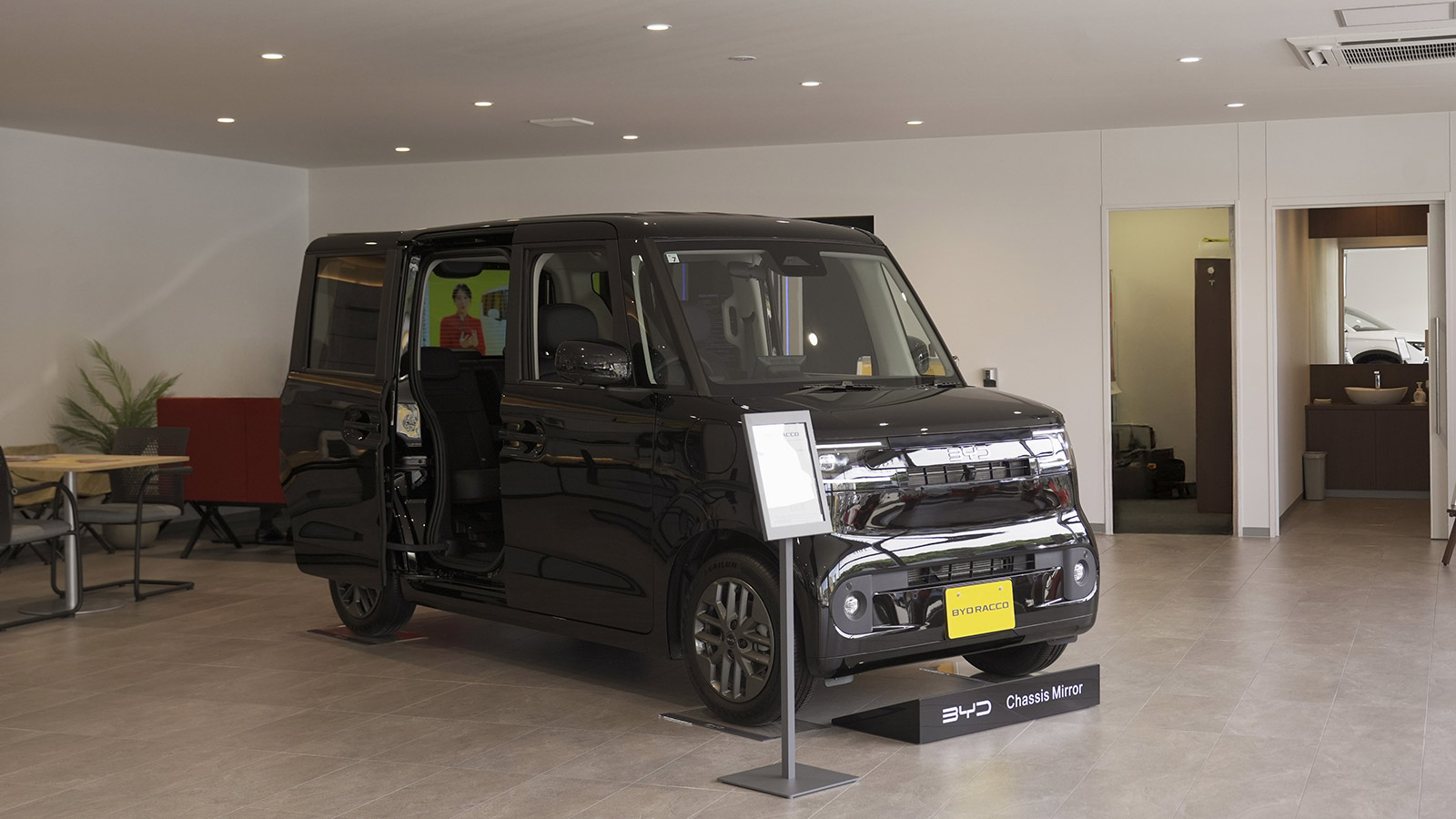 A black BYD Racco electric K-Car with its sliding door open at a BYD dealership in Japan.