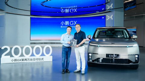 He Xiaopeng and Bu Xinwen pose with a commemorative display beside a silver Xpeng GX and large numerals reading "20000."