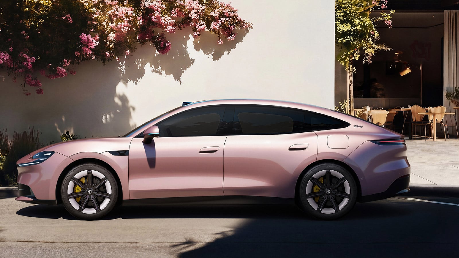 A pink MG 07 sedan shown in side profile outside a building decorated with flowering plants.