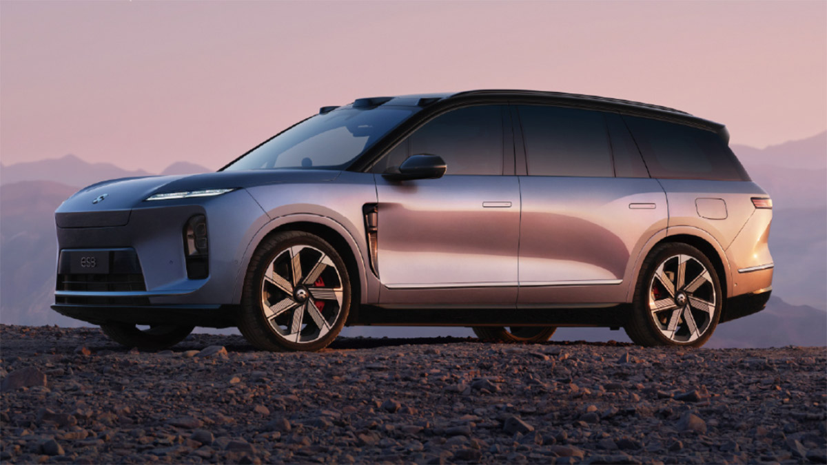 A third-generation Nio ES8 electric SUV parked on rocky terrain against a mountain backdrop at sunset.