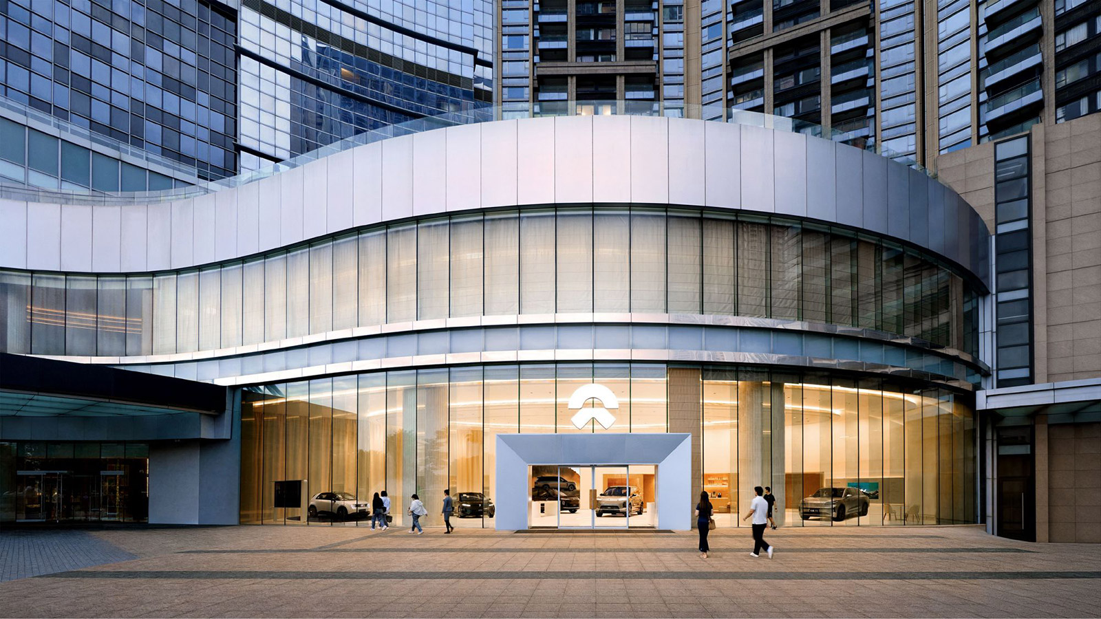 Exterior of Nio House Macau with a curved glass facade and several Nio vehicles on display.