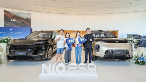 Customers and Nio representatives pose between 2 Nio ES9 SUVs during a vehicle handover ceremony in Macau.