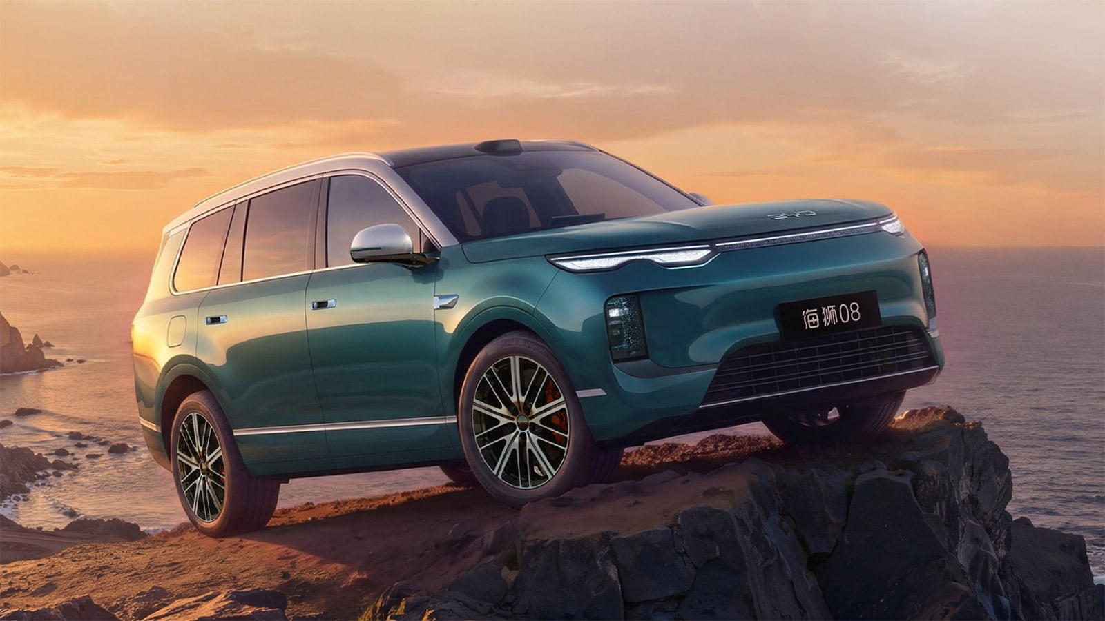 Green BYD Sealion 08 SUV shown from the front three-quarter angle on a rocky coastline at sunset.