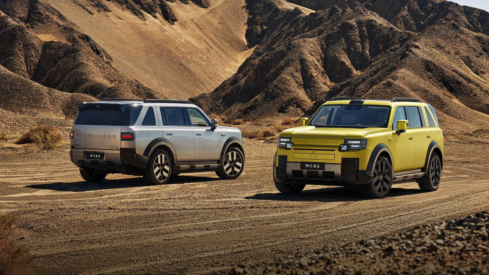 Two Freelander 8 SUVs in silver and yellow parked on rocky terrain against a mountainous backdrop.