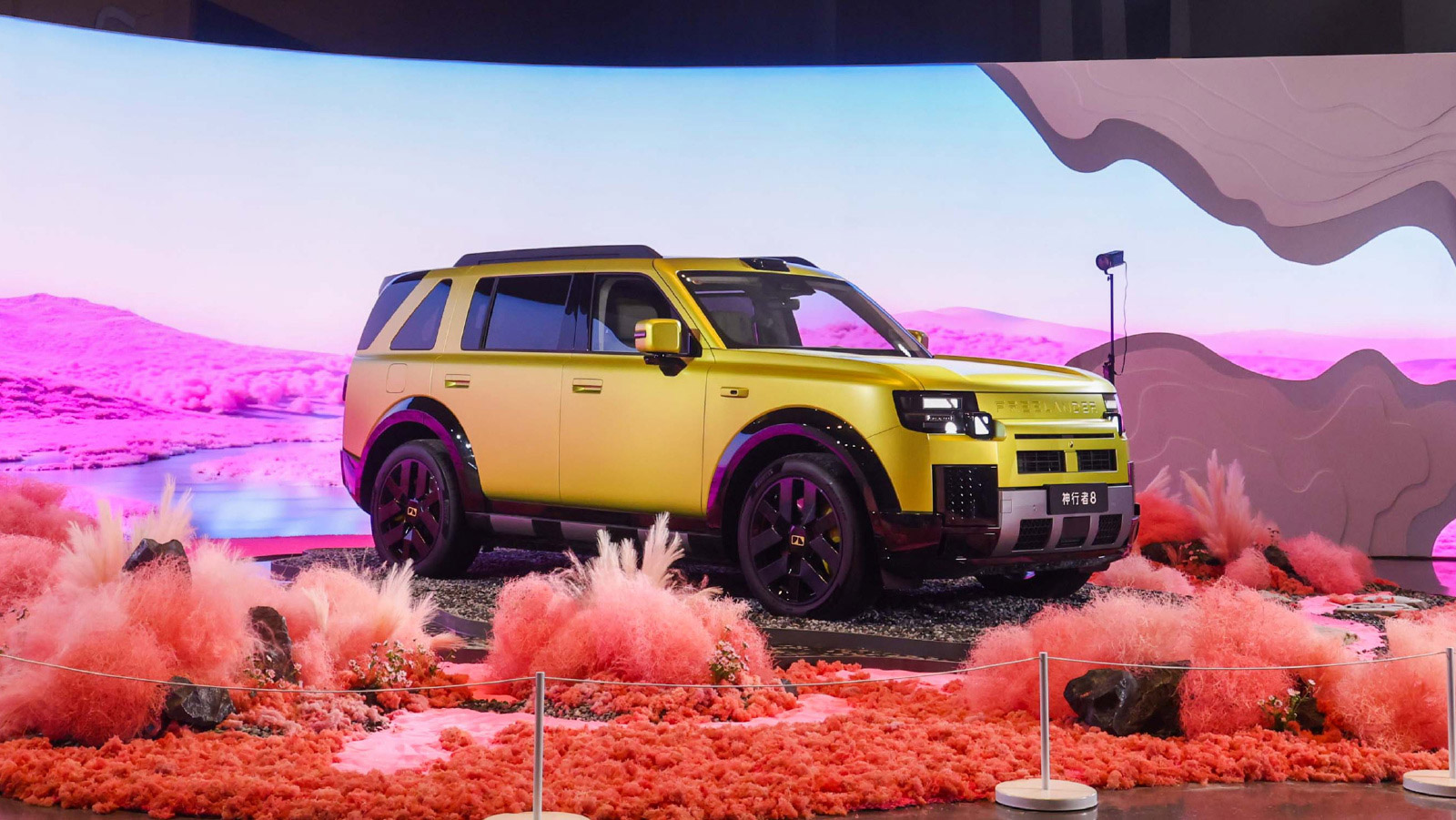 A yellow Freelander 8 displayed on a desert-themed stage with pink lighting and decorative plants.