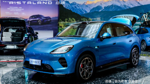 A blue Aistaland GX7 is displayed indoors with its tailgate open, alongside other GX7 SUVs configured with luggage and outdoor gear.