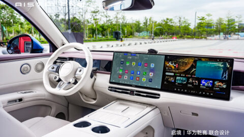 Interior of the Aistaland GX7 featuring a white steering wheel, dual 15.6-inch dashboard screens and a center console with cupholders.