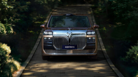 Front view of a Voyah Dream 9 driving along a tree-lined road, highlighting its large chrome grille and split headlights.