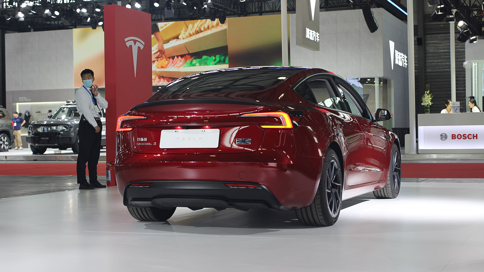 Rear three-quarter view of a red Tesla Model 3 on display at an auto show.