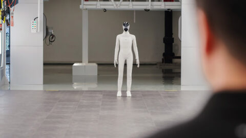 Xpeng's Iron humanoid robot stands across the factory floor as a person watches from the foreground.