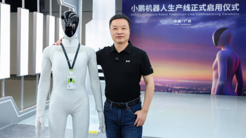 Xpeng chairman and CEO He Xiaopeng poses beside an Iron humanoid robot wearing a staff badge.