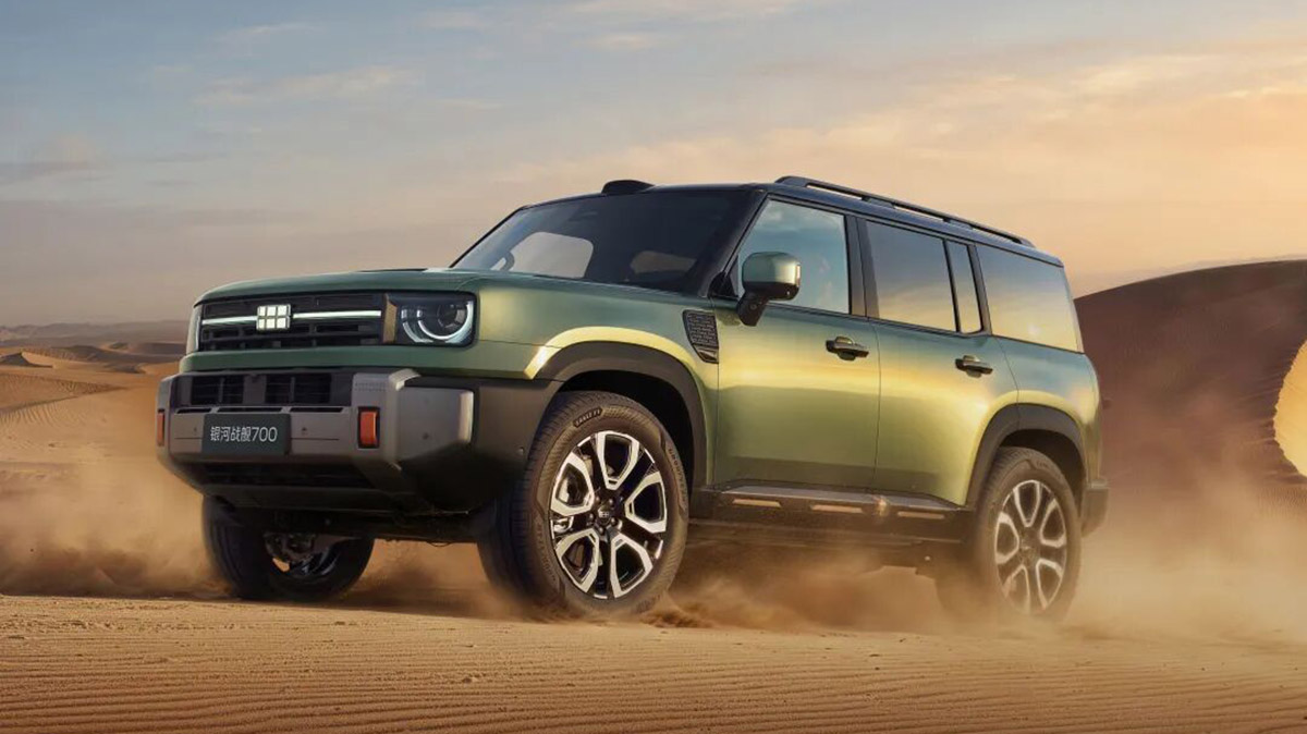 A green Geely Galaxy Cruiser 700 SUV driving across desert sand, viewed from the front three-quarter angle.