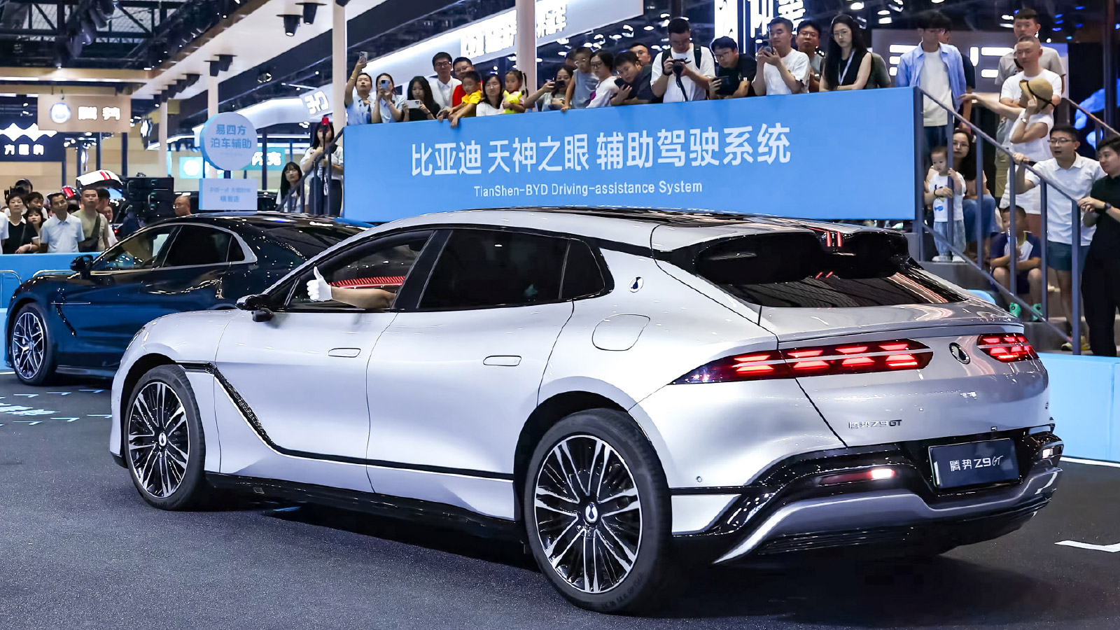 Rear three-quarter view of a silver Denza Z9GT at the Chengdu Auto Show, with spectators watching from behind a barrier.