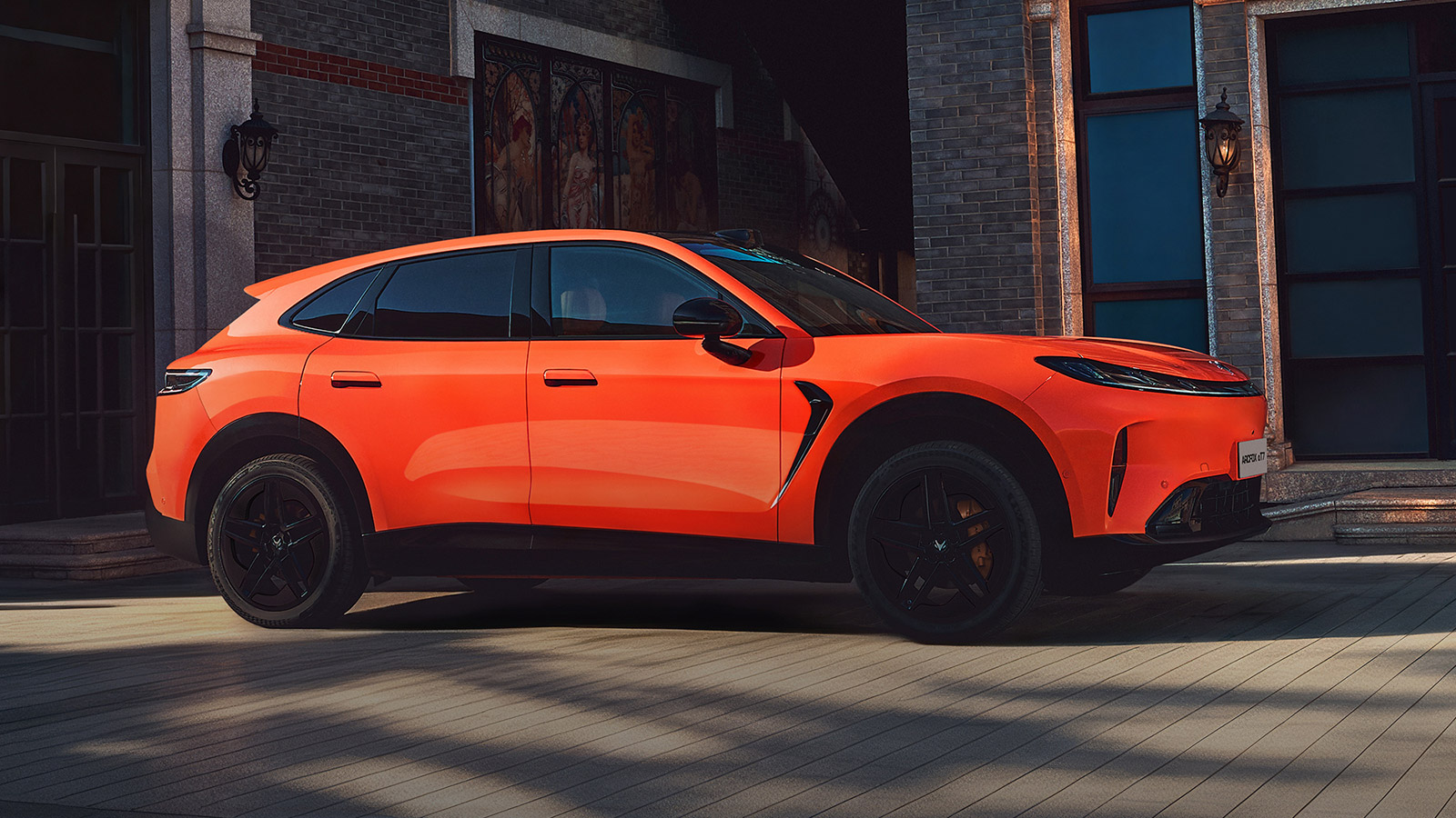 Orange Arcfox Alpha T7 SUV with black wheels, shown from the side and front outside a brick building.