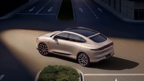 Elevated rear three-quarter view of a champagne-beige IM LS6 turning at an urban intersection.