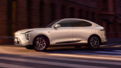 Side view of a champagne-beige IM LS6 driving along an urban street, showing its sloping roofline and flush door handles.