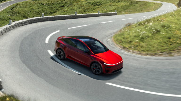 Red Tesla Model Y Performance taking a bend on a winding mountain road, viewed from above.