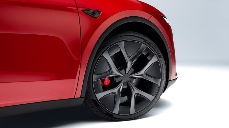 Close-up of a Tesla Model Y Performance front wheel, showing a dark alloy rim, red brake caliper and Pirelli tire.