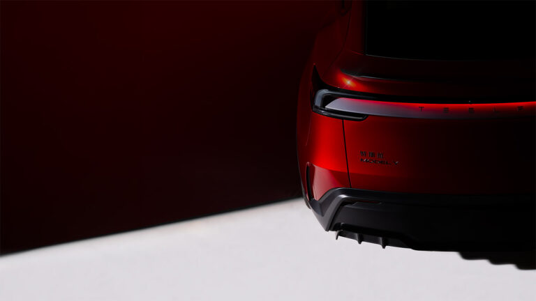Rear detail of a red Tesla Model Y Performance, showing its illuminated light bar, spoiler, Model Y badge and lower diffuser.
