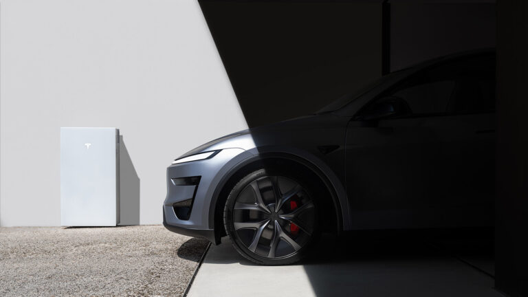 Gray Tesla Model Y Performance parked partly in shadow at a garage entrance, with its front wheel and red brake caliper visible.