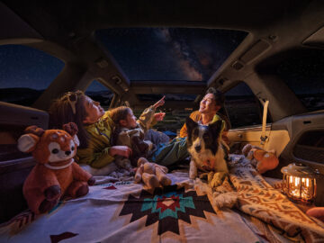 Family and dog relaxing inside an Onvo L80 beneath a panoramic glass roof with a starry sky overhead.