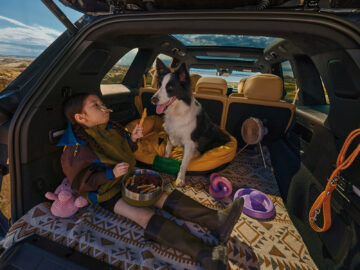 Child and dog sitting in the Onvo L80’s open rear cargo area, surrounded by pet toys and a portable fan.
