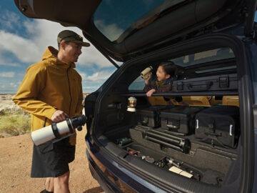 Onvo L80 rear cargo area loaded with outdoor equipment, with a man holding a telescope and a child holding binoculars.