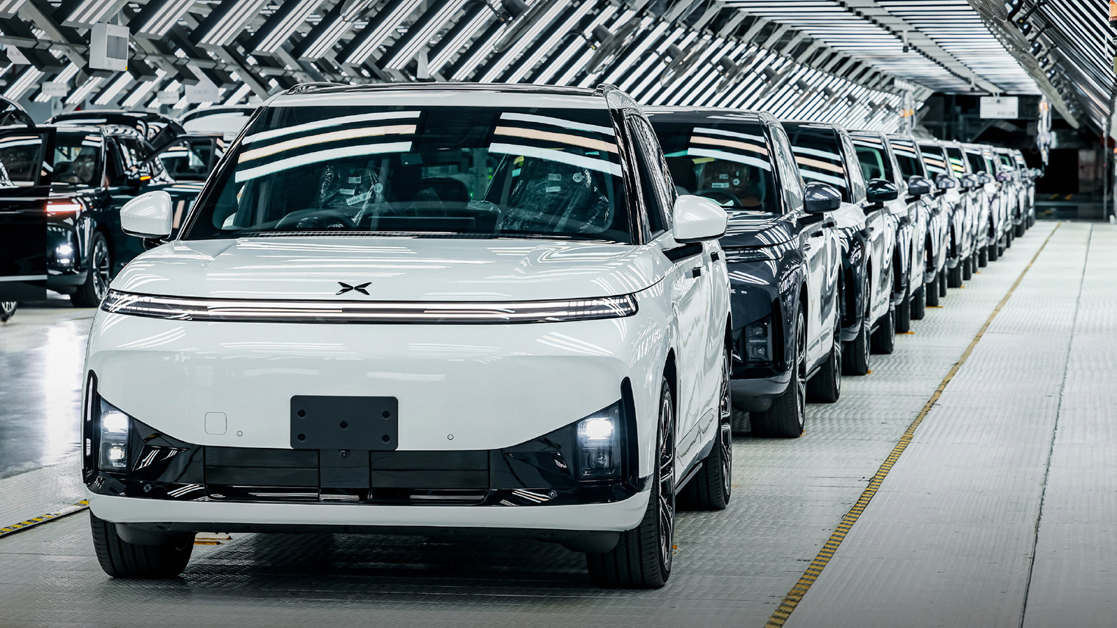 A white right-hand-drive Xpeng G9L leads a row of SUVs inside the company's Guangzhou factory.