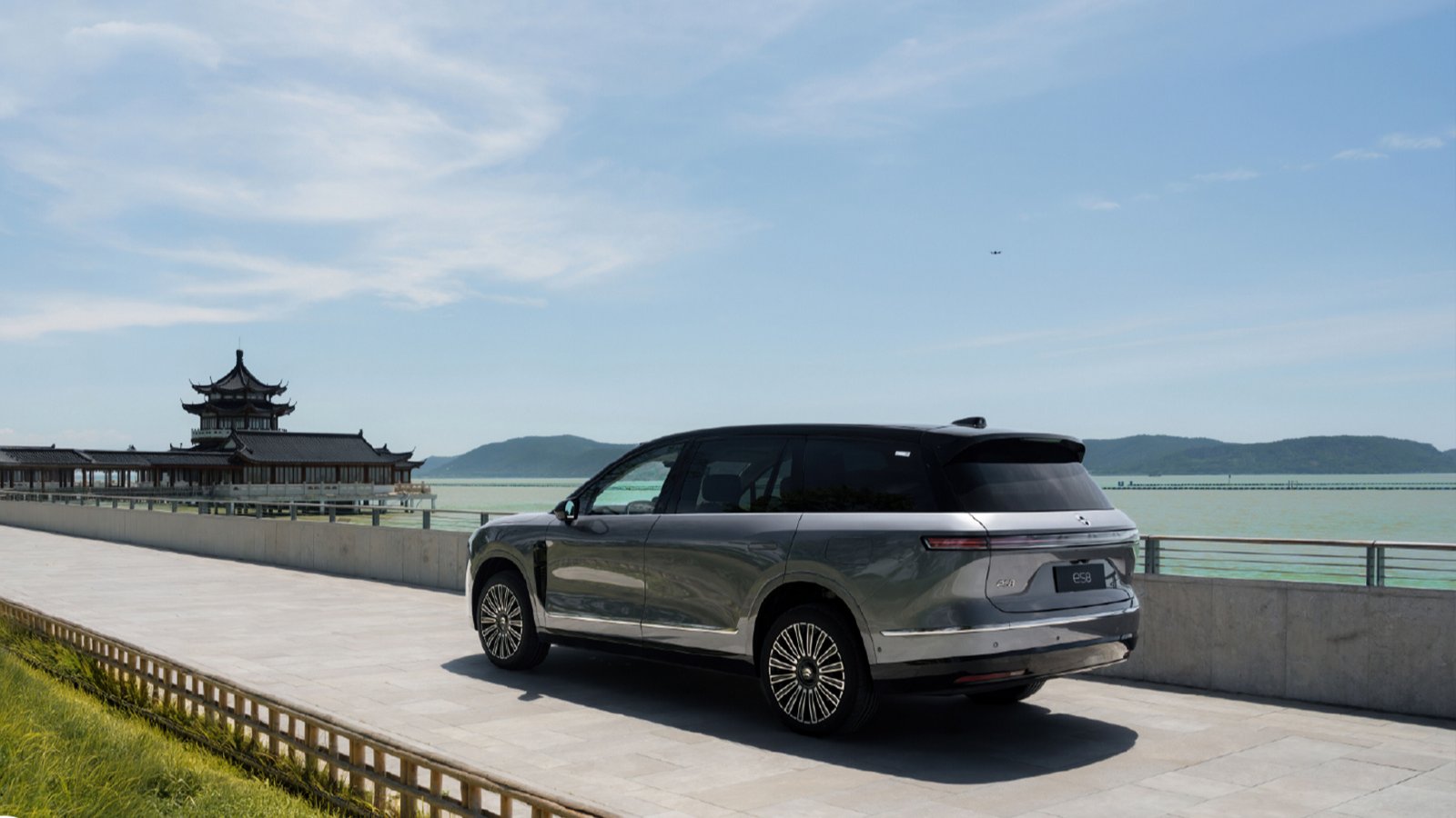 Rear three-quarter view of a gray third-generation Nio ES8 electric SUV by the water, with a traditional Chinese pavilion in the background.