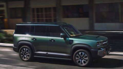Green Geely Galaxy Cruiser 700 driving along an urban road, showing its boxy profile, black roof rails, and side steps.