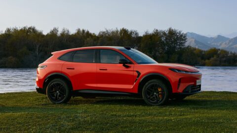 Side profile of an orange Arcfox Alpha T7 parked on grass beside a lake.