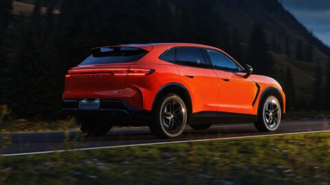 Orange Arcfox Alpha T7 driving along a mountain road, showing its rear light bar and roof spoiler.