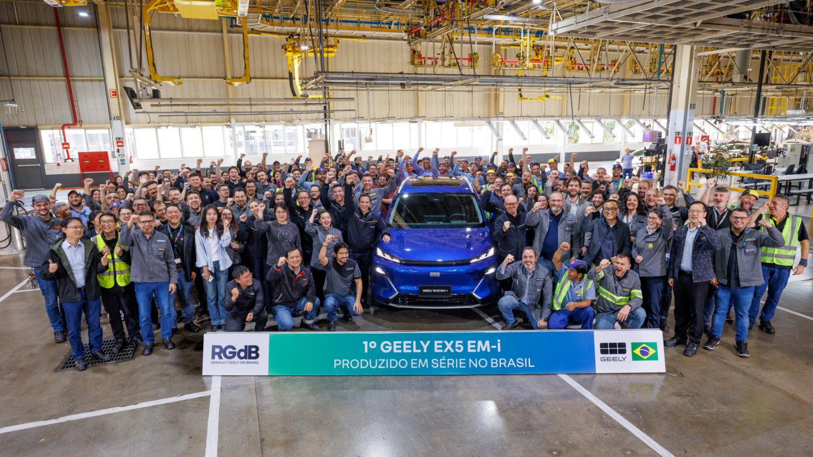 Workers gather around a blue Geely EX5 EM-i at the Ayrton Senna plant in Brazil to celebrate the start of local production.