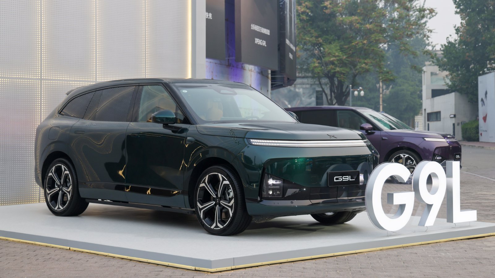 Green Xpeng G9L shown from the front three-quarter angle, with a purple G9L behind it and illuminated G9L lettering alongside.