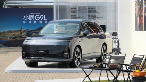 Gray Xpeng G9L displayed from the front three-quarter angle beside camping chairs and a table, with seat exhibits behind it.