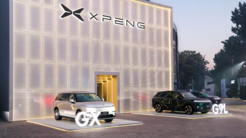 White Xpeng GX displayed alongside green and purple G9L SUVs outside an illuminated Xpeng exhibition building.