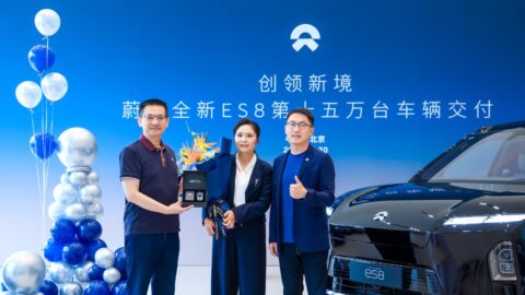Nio President Qin Lihong hands a Nio ES8 key box to owner Tang Limei, who holds a bouquet, while a Nio staff member gives a thumbs-up next to a black ES8 in front of a blue backdrop.