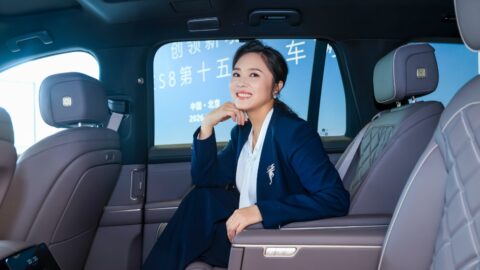 Tang Limei, wearing a navy blazer, smiles while seated in the second-row seat of a Nio third-generation ES8, with the delivery ceremony backdrop visible through the window.