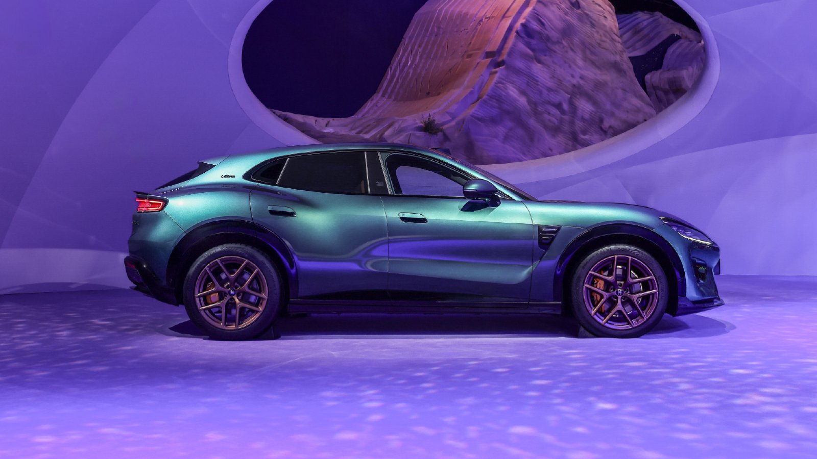 Side profile of a Luxeed RX coupe SUV in an iridescent green-to-purple paint finish with bronze multi-spoke wheels, displayed on a purple-lit stage in front of a large circular backdrop at the Chengdu auto show.