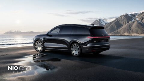 Black Nio ES8 viewed from the rear side, showing its Lanyue wheels beside the sea and rugged mountains.