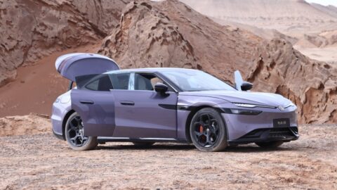 A purple Volkswagen ID. UNYX 09 parked on rocky desert ground in front of eroded sandstone formations, with its doors and rear trunk lid open, showing black wheels with red brake calipers and a slim front light bar.