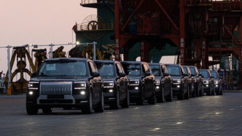 A line of black Zeekr 9X SUVs with headlights illuminated beneath port equipment.