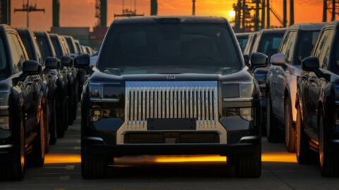 Front view of a black Zeekr 9X parked among rows of SUVs, with port cranes silhouetted against an orange sky.