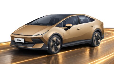 Front three-quarter view of a gold Hyundai Ioniq V electric sedan in motion, featuring a fastback silhouette, slim LED headlights, and a black roof.