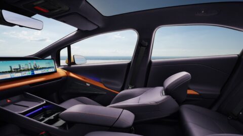 Side view of the Hyundai Ioniq V's interior, showing a reclined purple front passenger seat with leg rest, orange dashboard trim, a wide central touchscreen, and a panoramic glass roof.