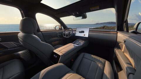 Interior of the Onvo L90 with the Mist Gray-themed luxury interior package, showing gray leather seats, a central touchscreen, a rear-seat display on the back of the center console, a panoramic glass roof, and a sea view through the windows.